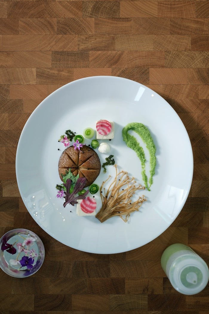 Elegant white plate with a beautifully plated meal sits on a dark wooden table, viewed from above.