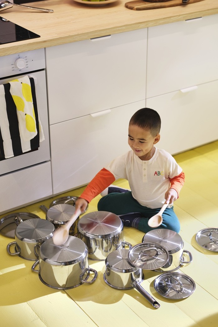 Child playing on the kitchen floor surrounded by IKEA 365+ pots and lids.