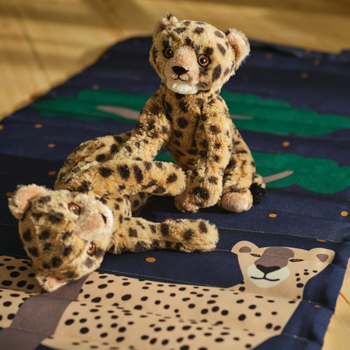 Two SANDLÖPARE soft toy cheetah cubs play on a dark blue and green rug decorated with a cheetah illustration.