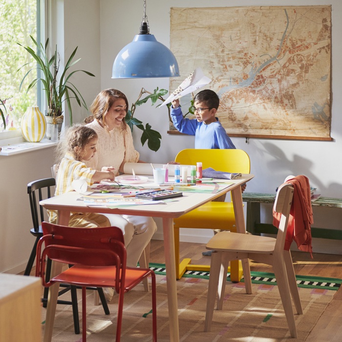 Family enjoying crafts and drawing together at a dining table surrounded with colourful chairs.