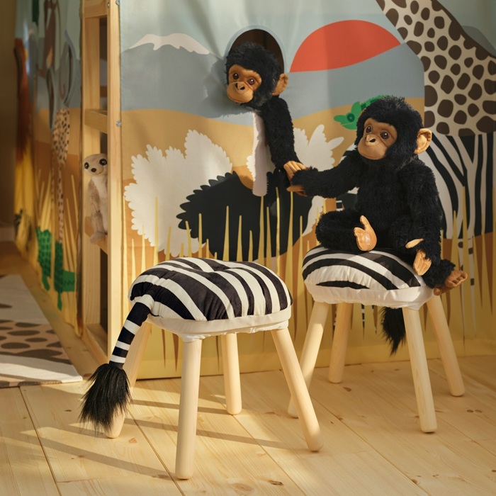 Two SANDLÖPARE soft toy chimpanzees play on stools decorated with giraffe-pattern stool covers with tails.