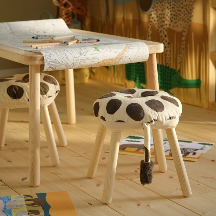 A children’s desk with two stools decorated with matching giraffe-pattern SANDLÖPARE stool covers.