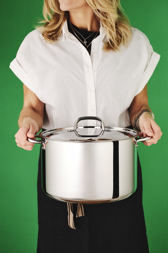 Person holding the IKEA 365+ stainless steel pot with lid against a green background.