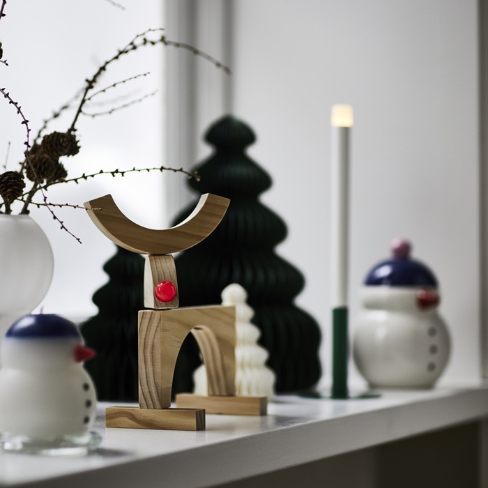 Светодиодная свеча STRÅLA мягко светится на подоконнике среди праздничных украшений и деревянных фигурок.