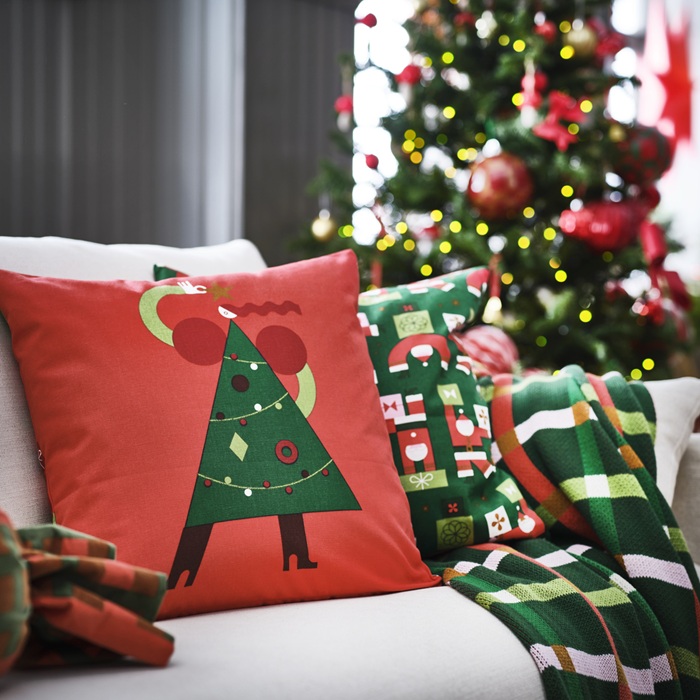 Диван с праздничными рождественскими подушками, украшенными рисунком в виде украшенной ёлки ​​и клетчатым узором в красно-зелёную цветовую гамму.