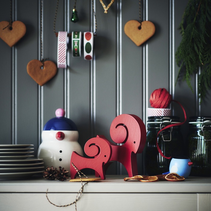 Праздничная композиция с традиционными скандинавскими деревянными украшениями в виде коз, пряничными сердечками и катушками лент на фоне обшитой панелями стены.
