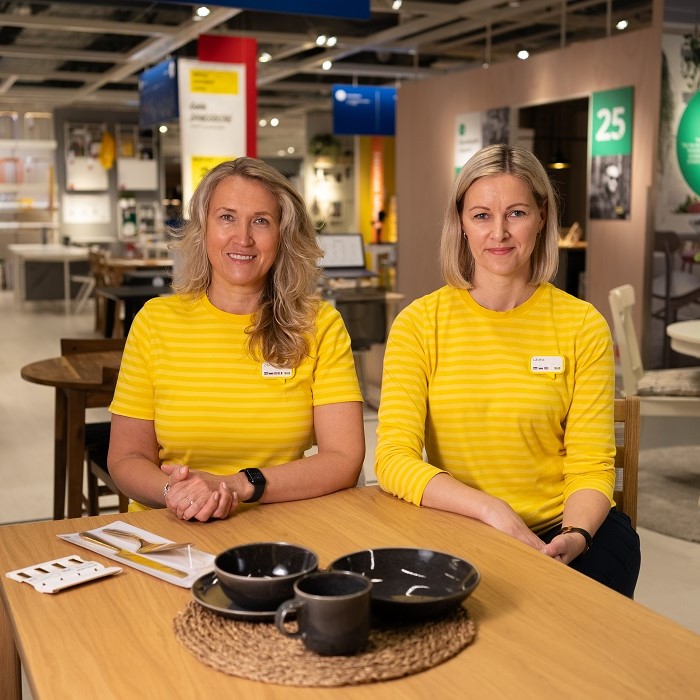 Divas IKEA ekspertes pie galda veikalā ar tumši pelēkiem GLADELIG traukiem uz pīta paliktņa.