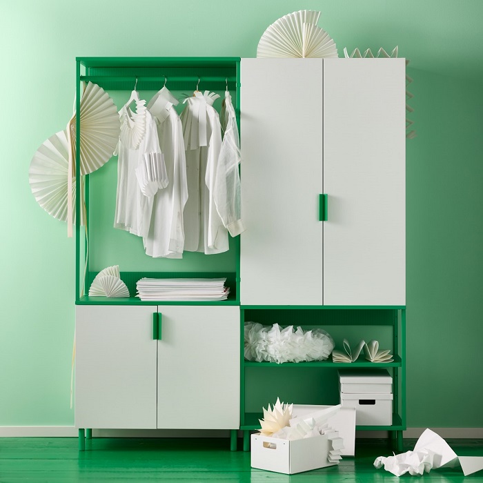 A modern white and green PLATSA wardrobe with open and closed sections. Inside, white clothes hang neatly, while the lower shelves hold storage boxes and decorative items.
