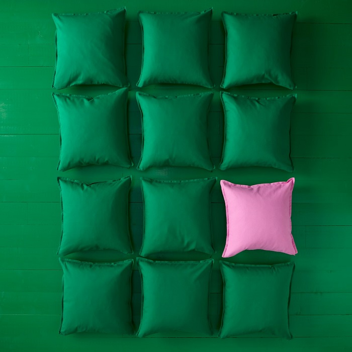 A collection of green GURLI cushions arranged in a grid on a green background, with one pink cushion adding a playful pop of colour.