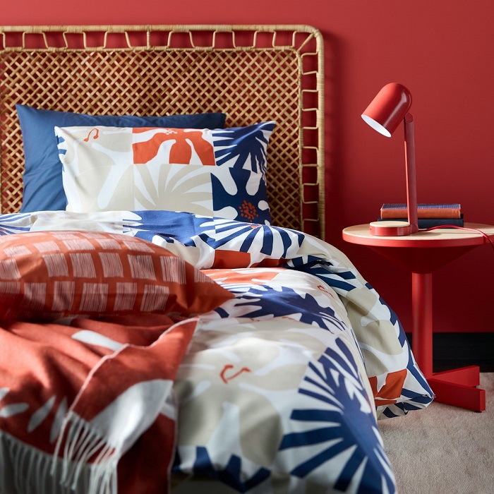 A HYLSNEJLIKA duvet cover set featuring a graphic pattern of flowers, paired with vibrant red and blue pillows, and a matching red bedside table.