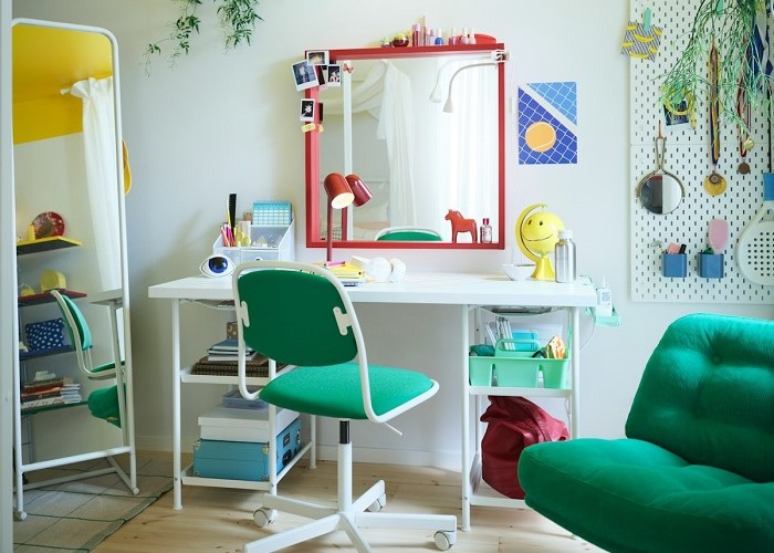 A bright children’s room with a white desk, green swivel chair, red-framed mirror, hanging plants, and a green armchair.