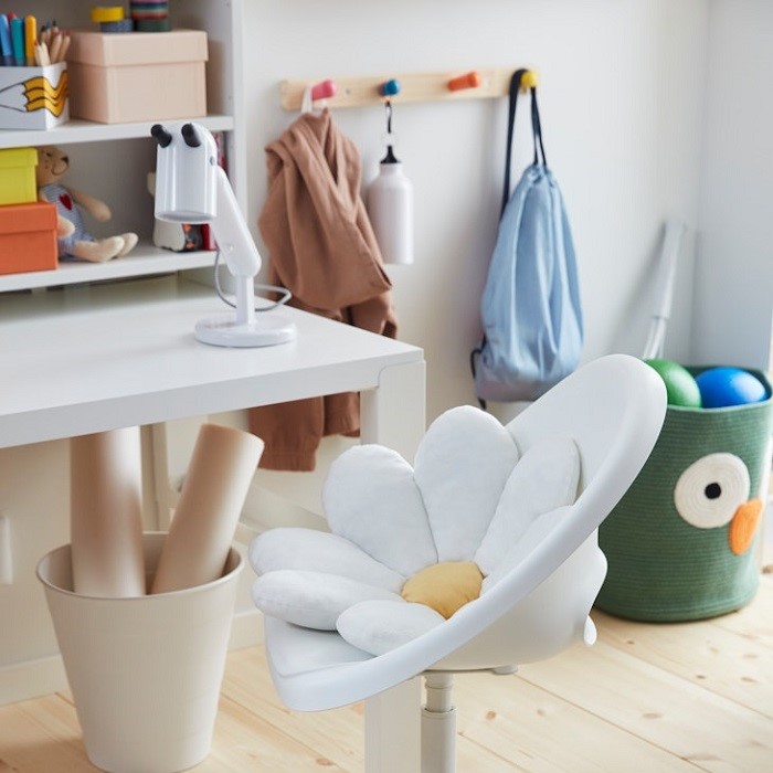 A white swivel chair with a daisy-shaped cushion on the seat, set in front of a desk, with wall hooks visible in the background.