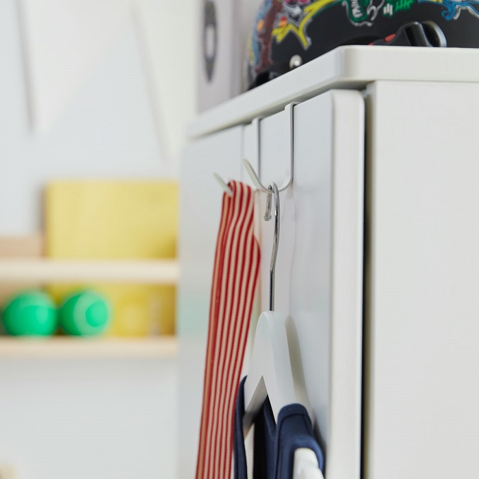 Two white hooks on a cabinet door—one holding clothes on a hanger, the other displaying a hanging medal strap.