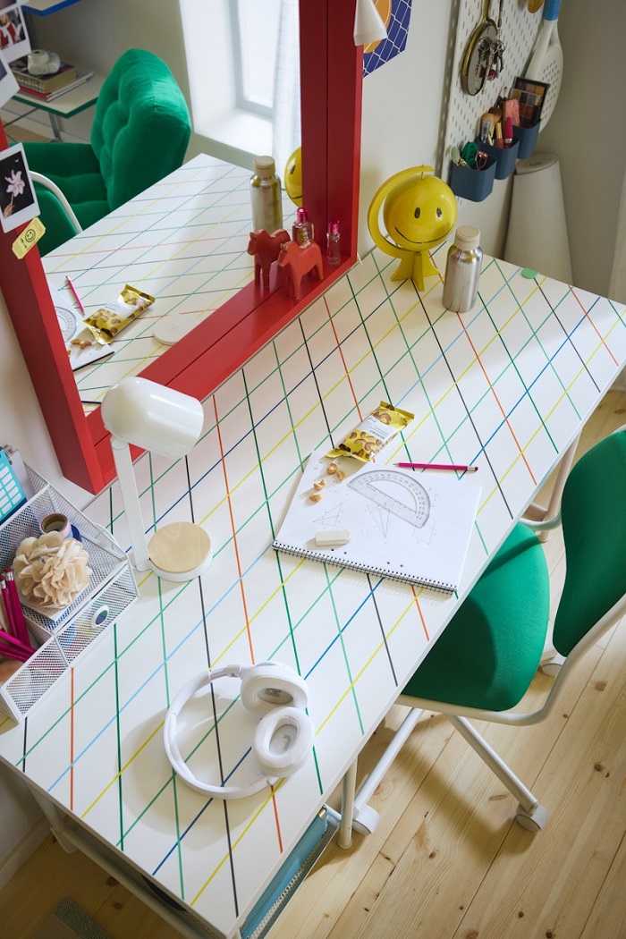 A playful desk featuring a multicoloured grid pattern, viewed from above, with headphones and a notebook placed on top.