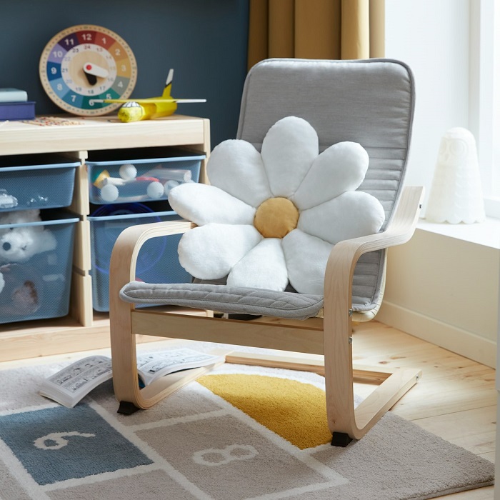 A light grey children's armchair stands in a kids' room, with a daisy-shaped cushion on it, and a patterned rug for playing hopscotch laid on the floor.