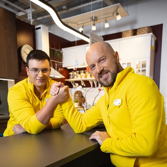 Du IKEA ekspertai su mėlynos ir geltonos spalvų uniformomis stovi parduotuvės erdvėje.