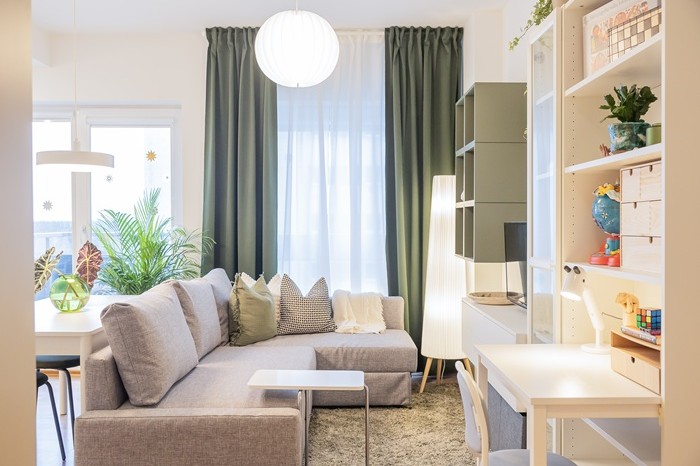 Modern living room with a grey sofa, green curtains and a home office area.