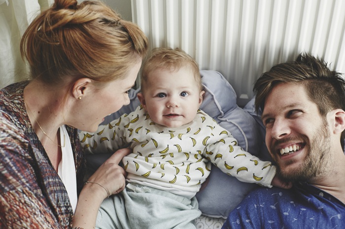 Smiling new parents, lying in bed, looking at their baby.