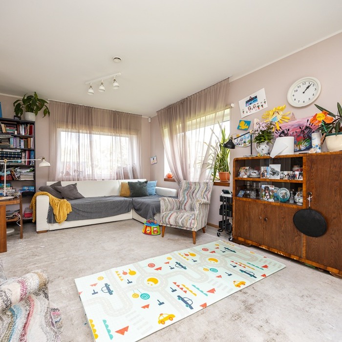 Big and airy living room full of mismatched items of furniture, toys and children´s drawings. There´s a play area in front and a white sofa on the background. 