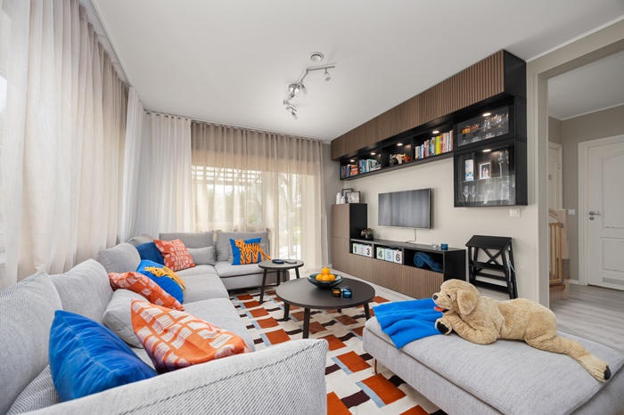 A beige and grey living room with splashes of blue and orange where the focus is on the  BESTÅ  wall shelf system.