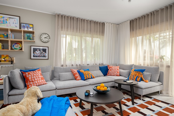 A beige and grey living room with splashes of blue and orange where the focus is on the big grey sofa with a sofa table and a big STOCKHOLM carpet. 