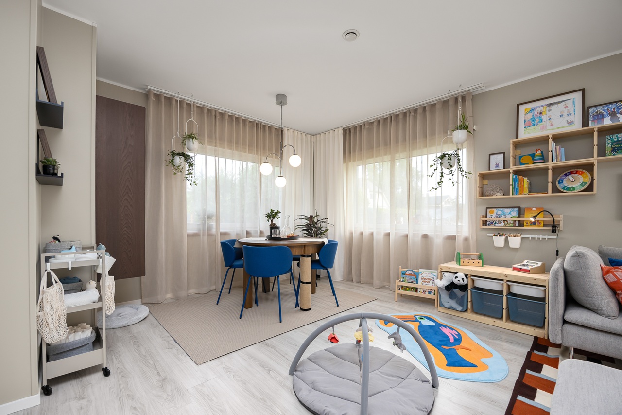 A dining area in a beige and grey living room with a play mat and play area on the foreground. Blue and orange details make the room livelier. 