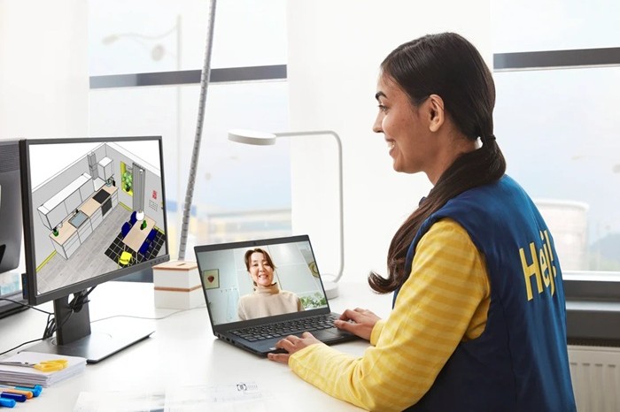 IKEA kitchen planning specialist in blue-and-yellow uniform is attending a video call, while a second screen displays a kitchen plan.