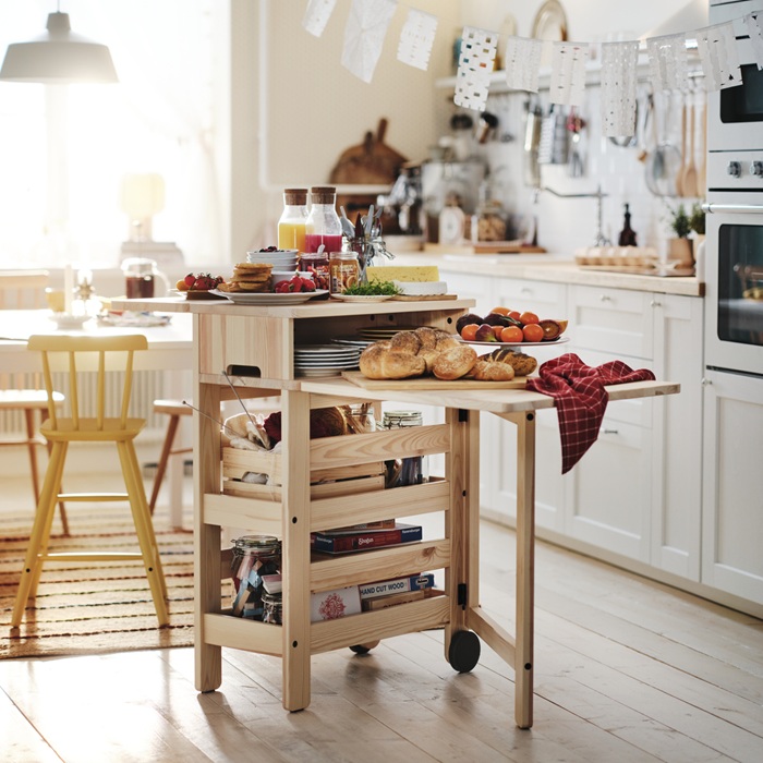 A wooden trolley filled with breakfast items is standing next to a dining table.