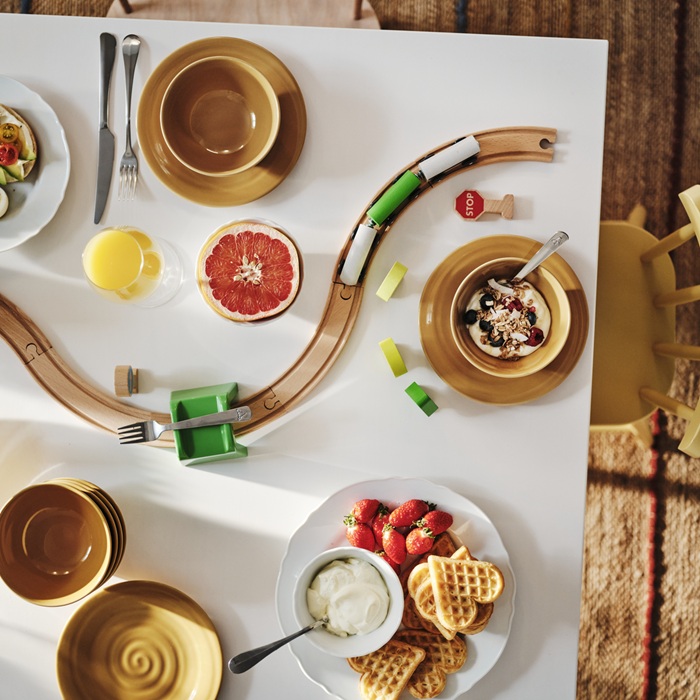 Tabletop with breakfast dishes and a toy train set running through it.