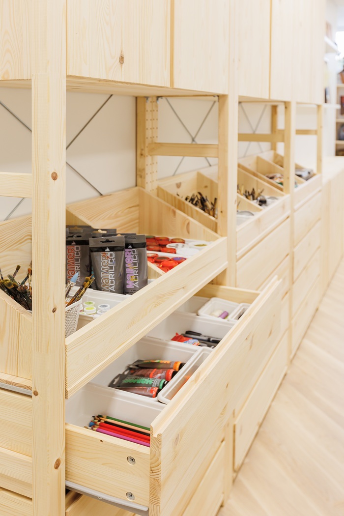 Mediniuose stalčiuose tvarkingai sudėti dažai, teptukai ir kitos kūrybos priemonės.