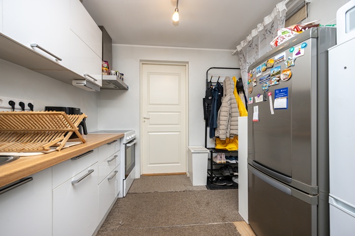 Vaade kitsasse kööki, mille parema seina ääres on kaks külmkappi ja vasakus küljes köögikapid. Ruumi kaugemas otsas on valge uks.