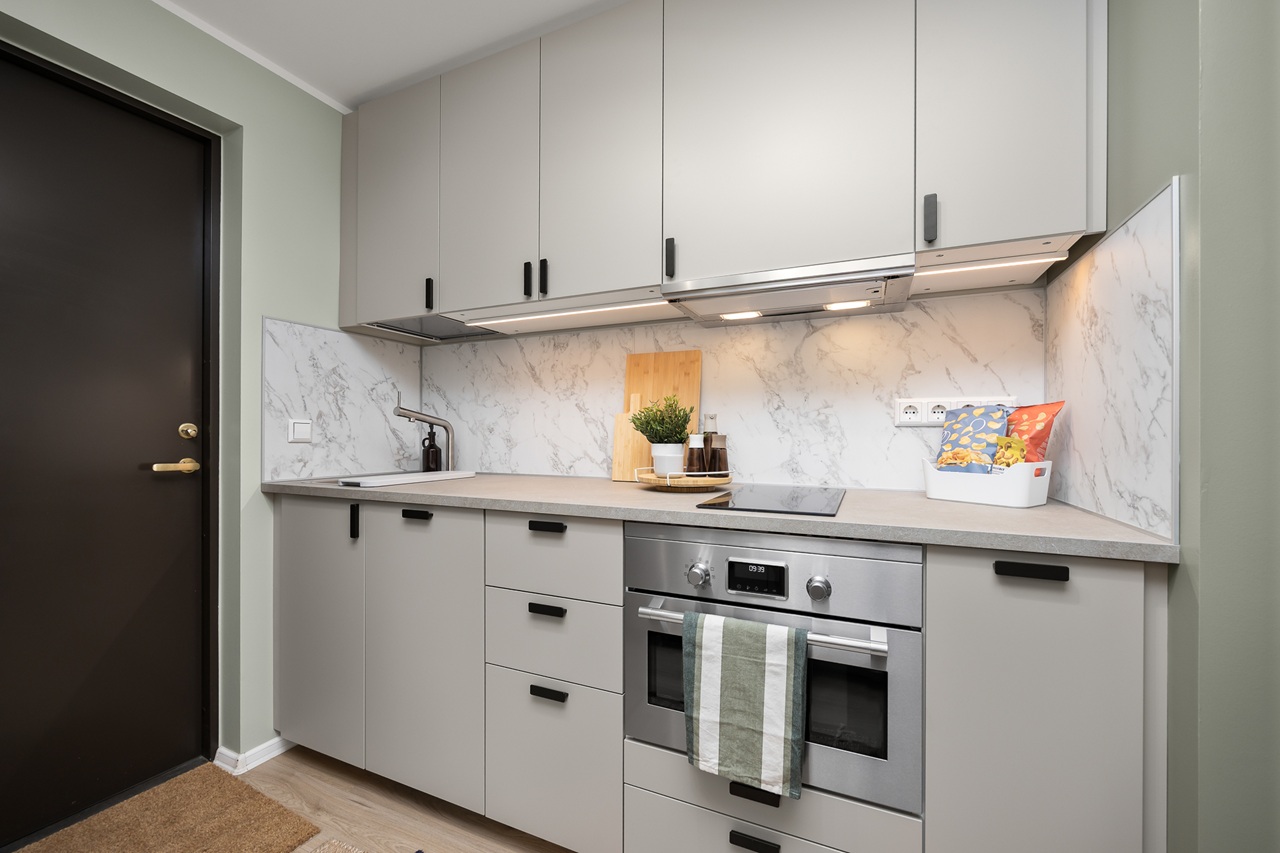 Vaade üherealisele köögile, mille ülemised ja alumised kapid on hallid. Tagasein on marmorplaat. Vasakus servas on valamu, keskel all ahi.