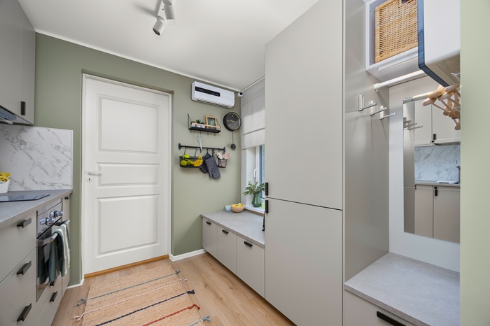 Vaade, mille keskpunktis on ruumi esikuosa. Ees paremal on riidepuutoru riidepuude jaoks, paremal keskel on külmkapp ja paremal tagaservas akna all madal tasapind, millel saab istuda.