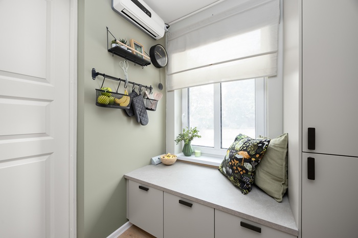 Aken, mille all on madal pind, mille all on sahtlid kingadele ja köögitarvetele. Seinal reelingul on hoidikutes köögitarvikud. Sein on hallikasroheline, sahltite esipaneelid on hallid. 