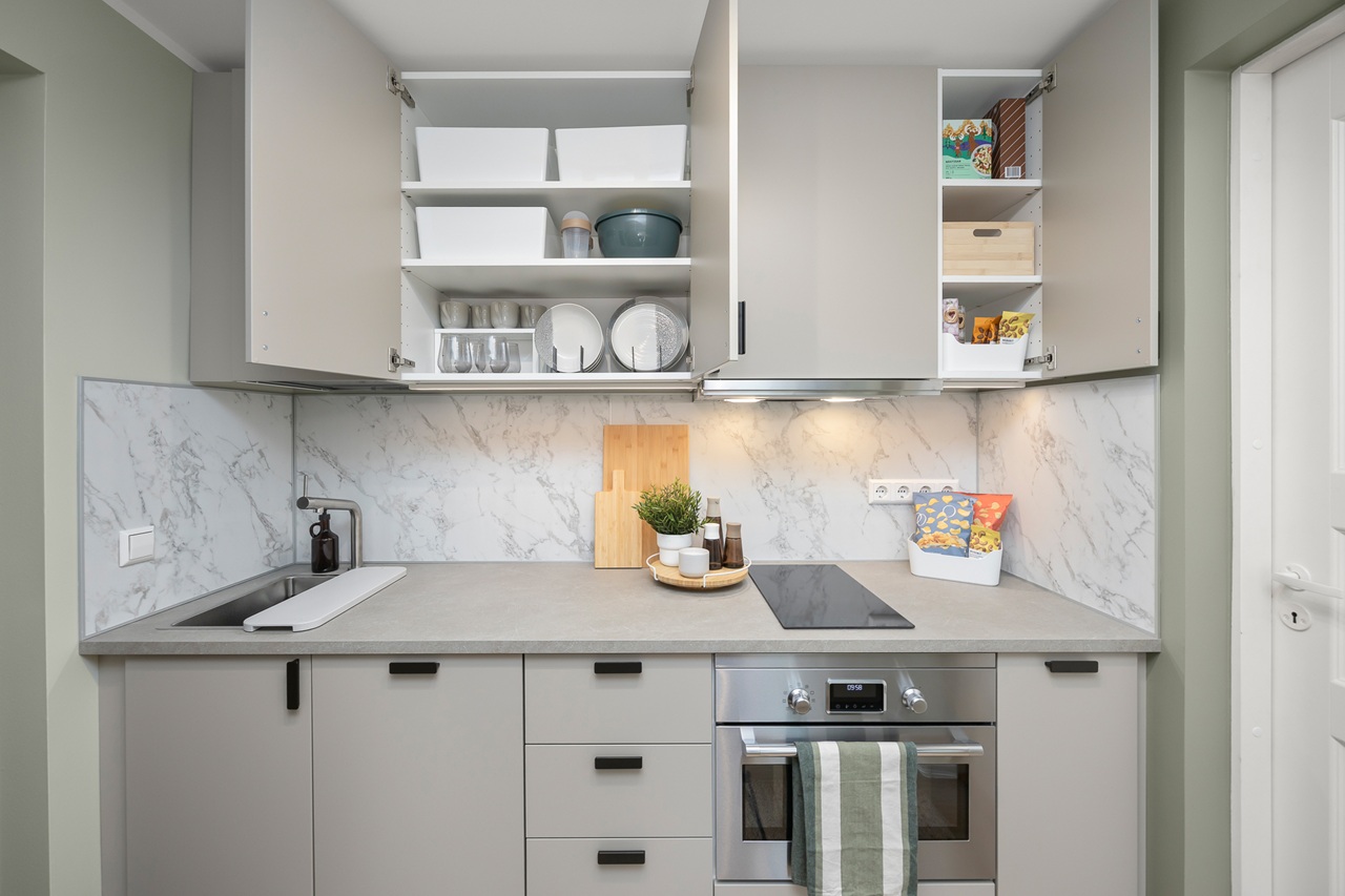 Vaade hallile üherealisele köögile, mille ülemiste kappide uksed on lahti, nii et sealt paistavad nõud ja kuivained.