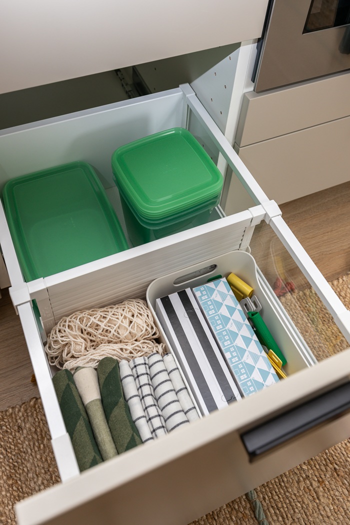 Ülaltvaade avatud köögisahtlile, kus on rohelise kaanega toidukarbid ja köögirätikud.