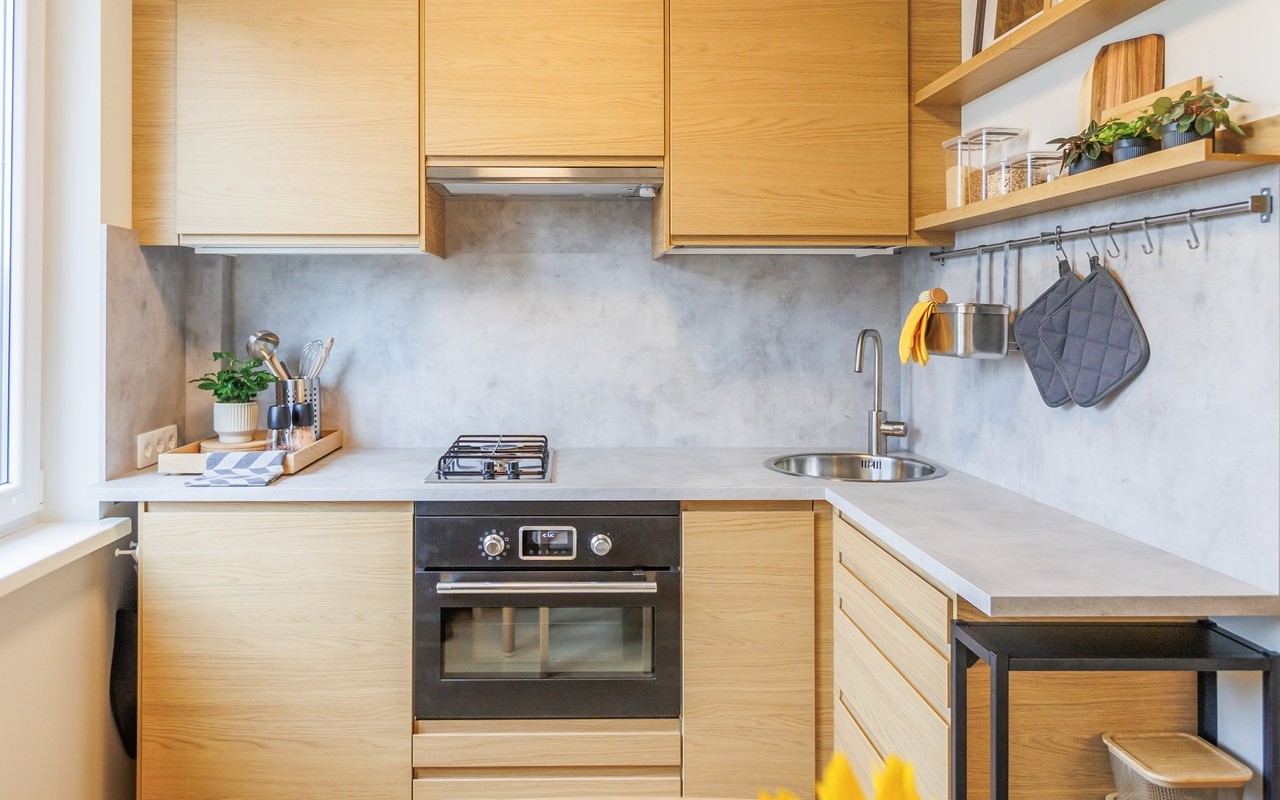 Jauki, šiuolaikiška virtuvė po atnaujinimo: spintelės su šviesios medienos fasadais, įmontuojamoji orkaitė, tvarkingas stalviršis, atviros lentynos ir modernūs akcentai.