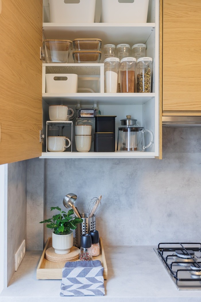 Sieninė spintelė su praviromis durimis. Viduje matosi tvarkingai sudėti stiklainiai, indai ir kiti virtuvės reikmenys.