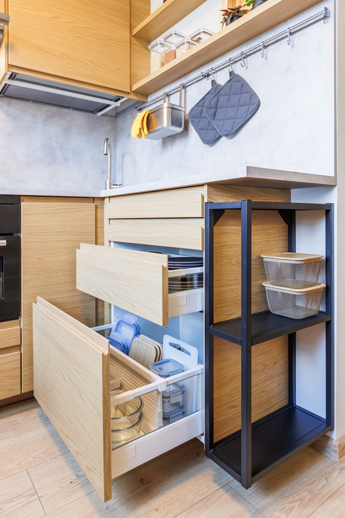 Ištrauktas virtuvinis stalčius, kurio viduje įrengta tvarkinga daiktų laikymo sistema su skyreliais biriems maisto produktams ir įvairiems rakandams.