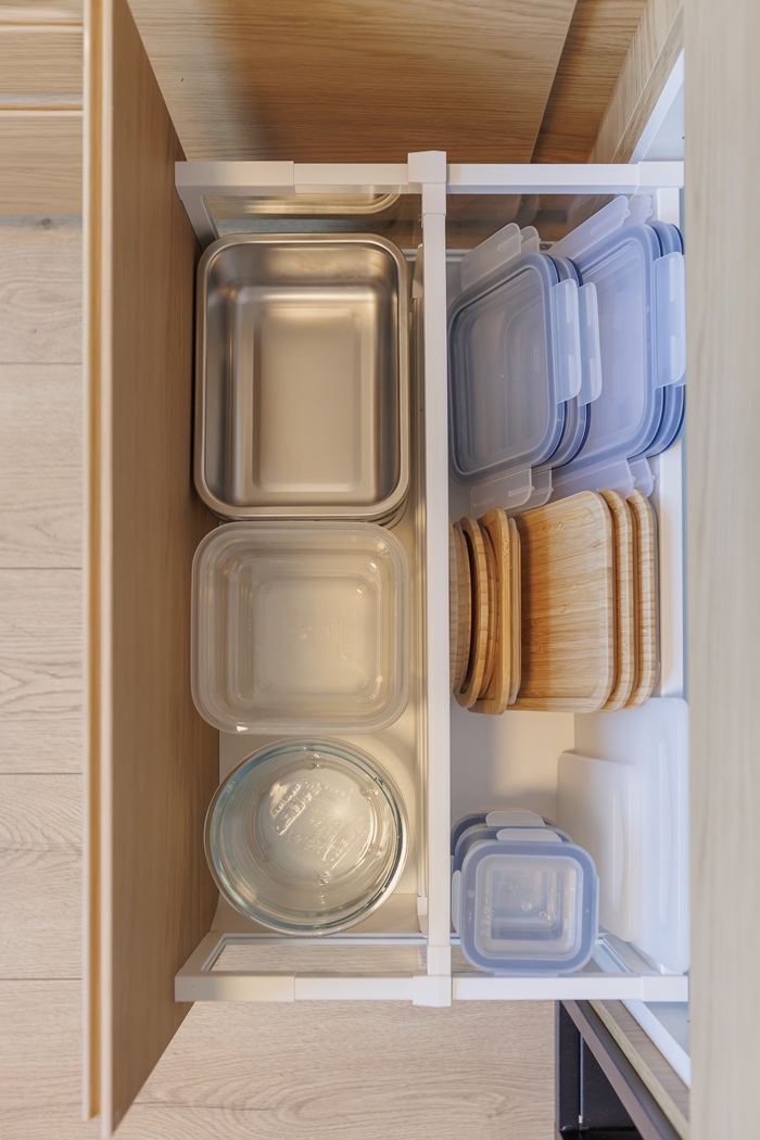 Vaizdas iš viršaus į gilų virtuvinį stalčių, kuriame tvarkingai sudėti maisto indeliai ir jų dangčiai.