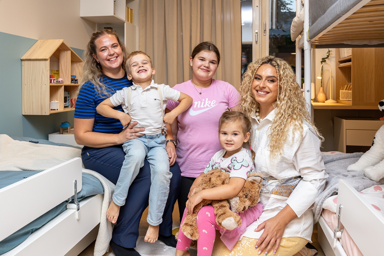 IKEA disainer ja telesaatejuht koos lastega istuvad värskelt sisustatud toas, kõigil on väga rõõmsad näod.