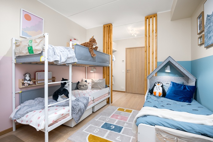 Vaade akna alt. Vasakule seina jääb valge metallist narvoodi, paremale seina sinise voodipesuga valge lapsevoodi. Vaibale on joonistatud keksukast.