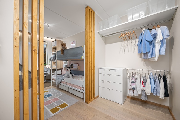 Valge seinaga garderoob, kus on valge kummut, mille ühel küljel ja kohal ripuvad riidepuutorul riided.