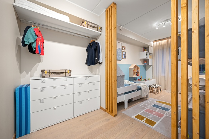 Garderoob, kus on valge kummut, mille ühel kohal ripuvad riidepuutorul riided. Kummuti kõrval on kokkupandud mängumatt.