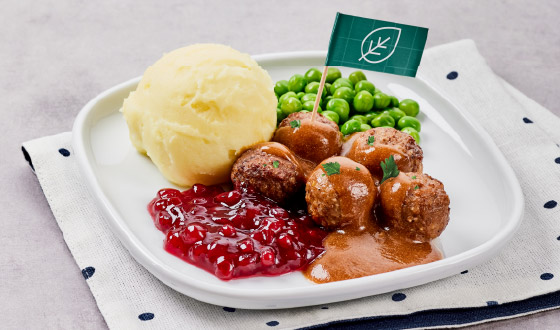 Четыре мясные фрикадельки с соусом, картофельным пюре и зелёным горошком на белой тарелке.				