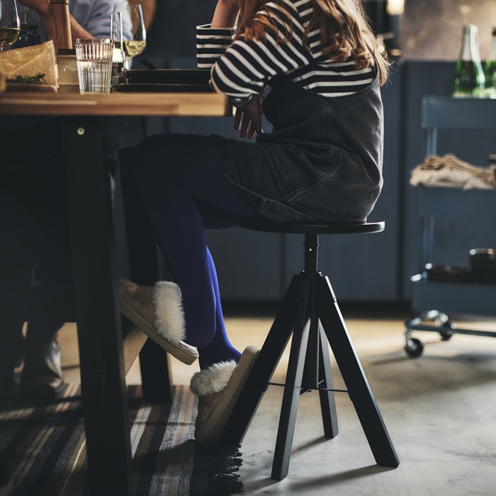 A person sitting at the table on a modern black RUDSTORP stool with a rotating seat.