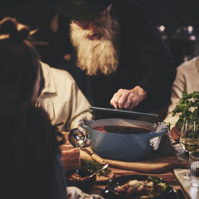 A person holding the lid of a VARDAGEN enamelled cast-iron casserole filled with food.