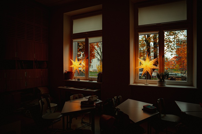 A view through a dim classroom to two windows with the STRÅLA stars shining on the windowsills.