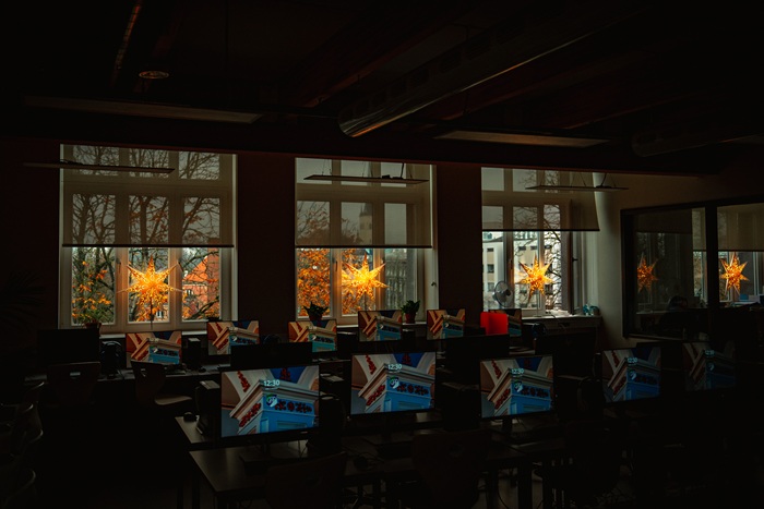 A view through a dim classroom to three windows with the STRÅLA stars shining on the windowsills.
