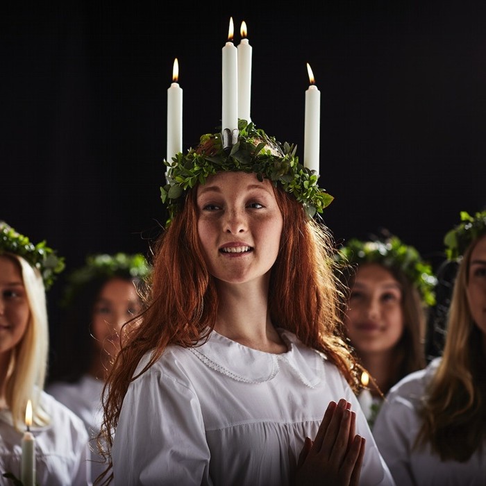 Baltās drānās tērpušās jaunas sievietes ar zaļiem vainagiem galvā, kas piedalās svētās Lūcijas dienas svinībās. Vienai no viņām galvā ir vainags ar svecēm.        